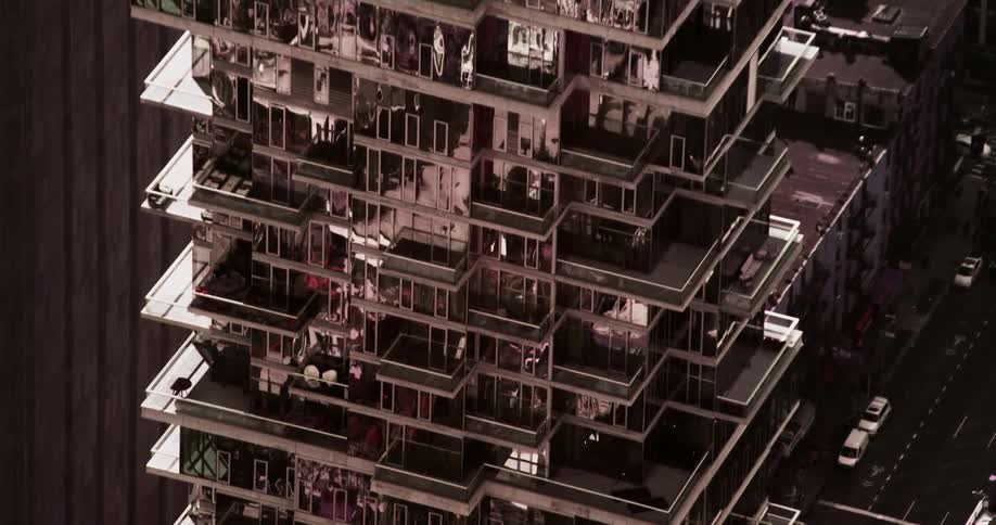 The window glass of an apartment highrise reflect the surrounding buildings in a city