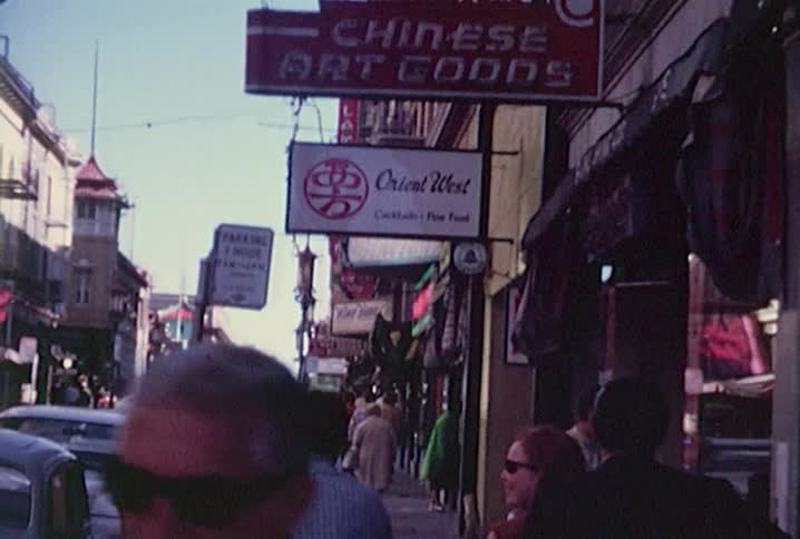 Old footage of people walking down a busy urban street lined with shops and restaurants