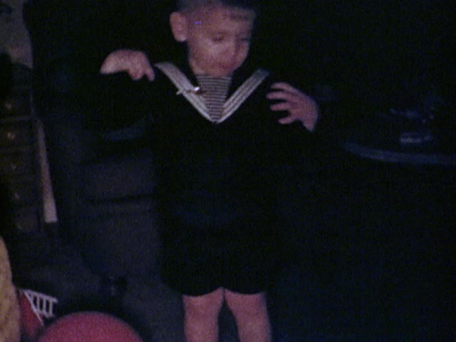 Old footage of a toddler dropping a large red ball and turning to play with a fire truck