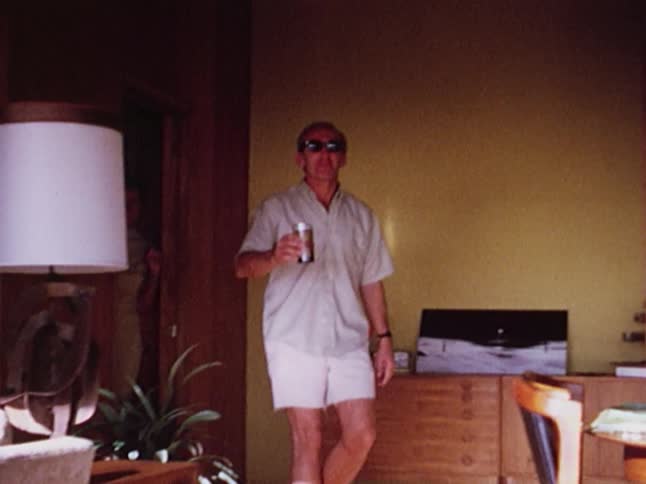 A man walks into a room smiling and waving