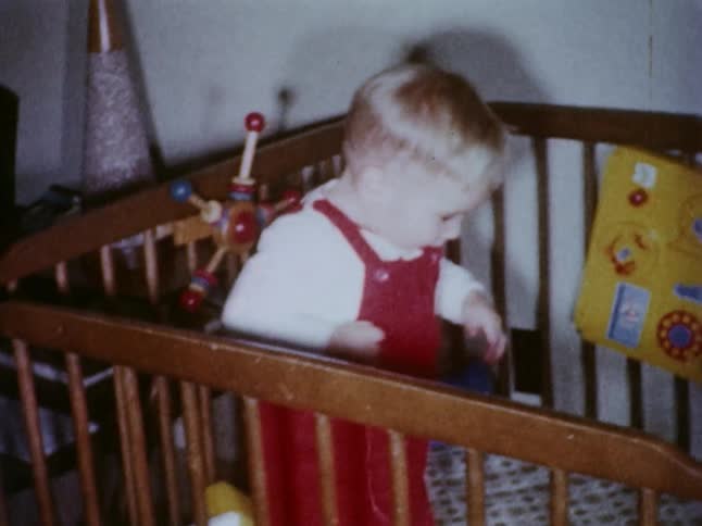 A toddler standing in his crib looking at the camera