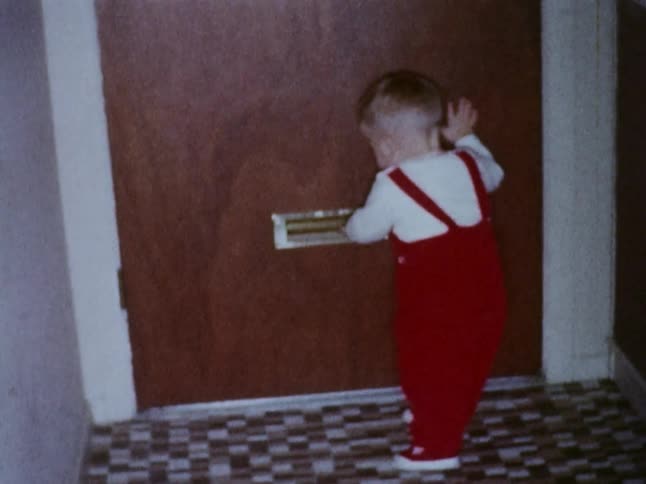 A little boy in red overalls walks around