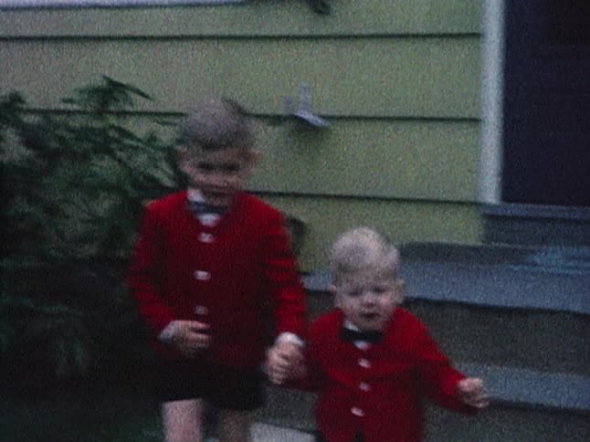 Old footage of two little boys in red sweaters walking away from a house while the older boy holds the younger boy's hand