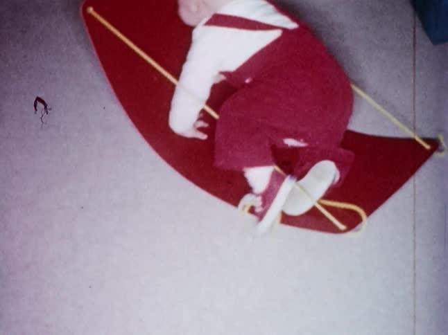 Old footage of a toddler climbing onto an old sled that rocks