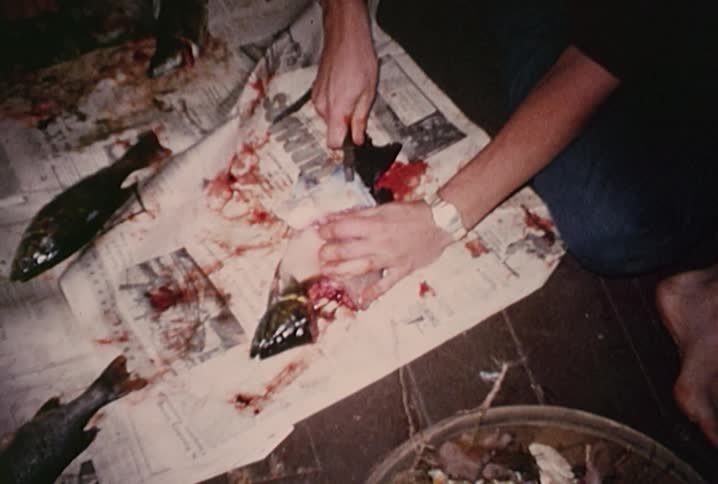 A man is skinning a fish on a table covered with newspaper