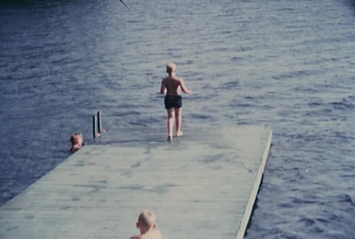 A boy running to the edge of a dock and dipping his foot into the water