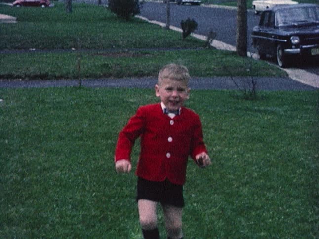 Old footage of a little boy standing on the sidewalk in a neighborhood before he starts to run towards the camera