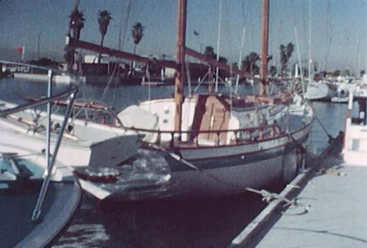 Old footage of a little boy standing on a pier near a boat located in a harbor where numerous boats are docked