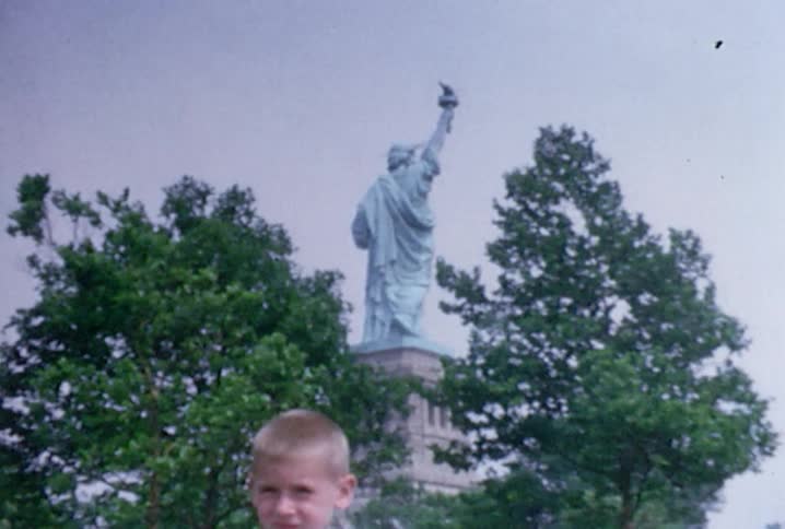 Old footage of a young boy with trees and the statue of liberty behind him
