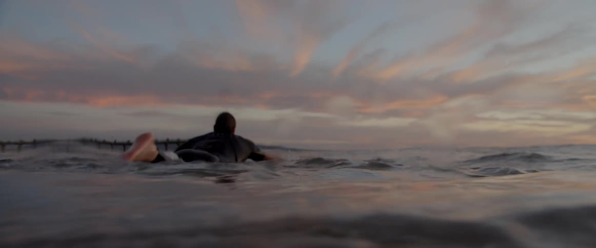 A male surfer paddles across the surface of the ocean atop his surfboard