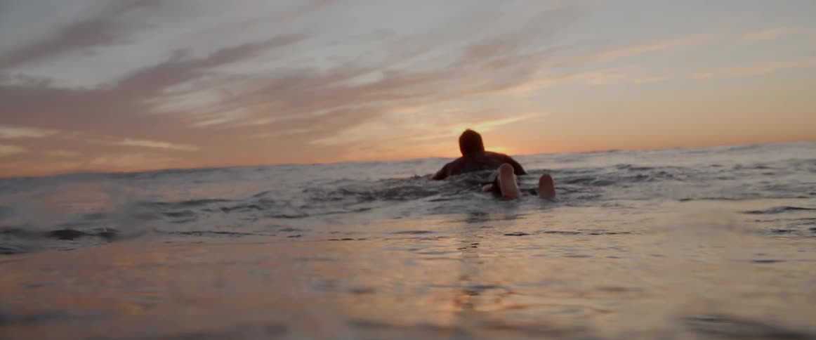 Close up view of surfer paddling in the ocean at sunrise