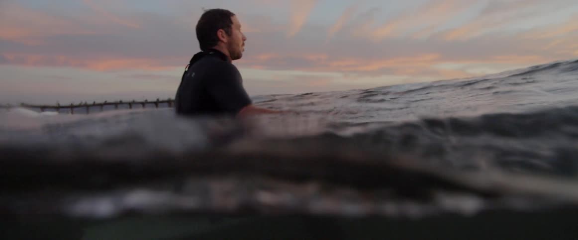 A man with a wetsuit sitting on a surfboard thats underneath the water