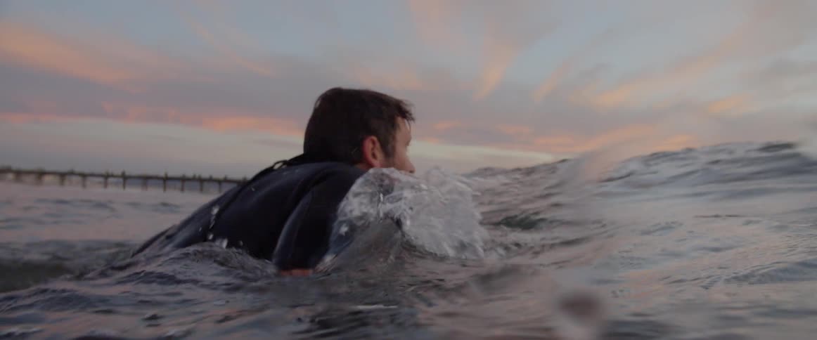 A man gets on his surfboard and starts paddling