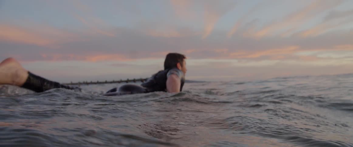 Close up of male surfer paddling in the ocean at sunrise