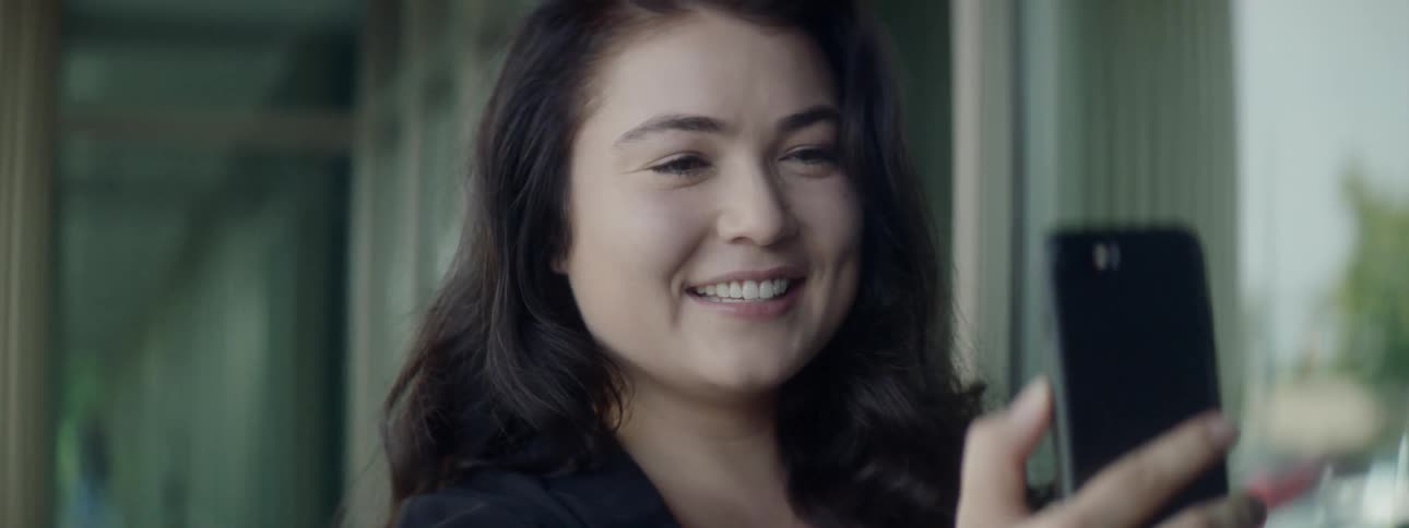 A young woman smiles and laughs while having a video chat with someone via her smart phone