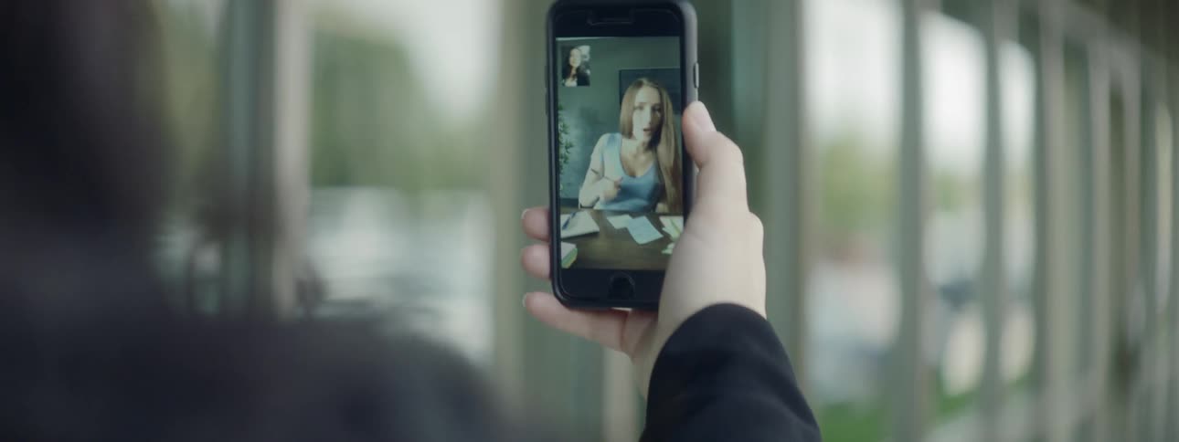 A person holds a cell phone in front of their face having a video call