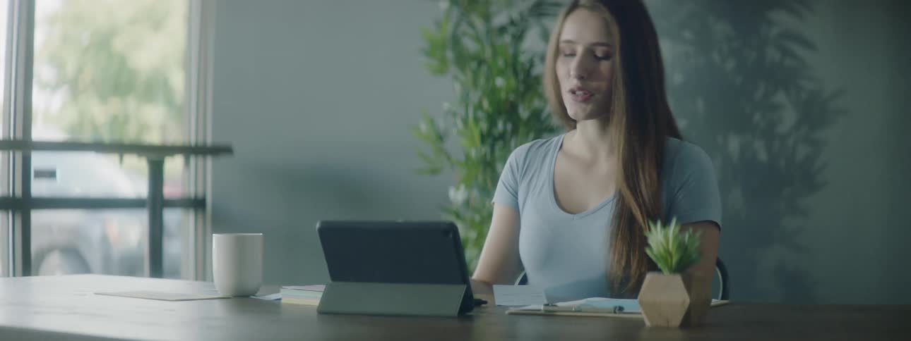 A woman is sitting at a table with her tablet computer and coffee cup