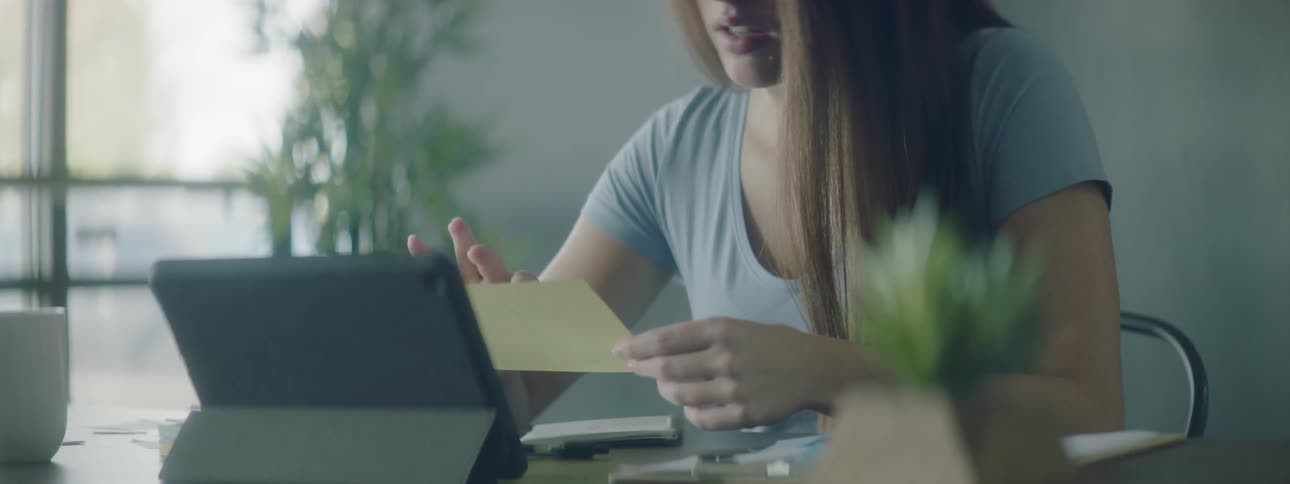 Woman review paper at table in front of tablet