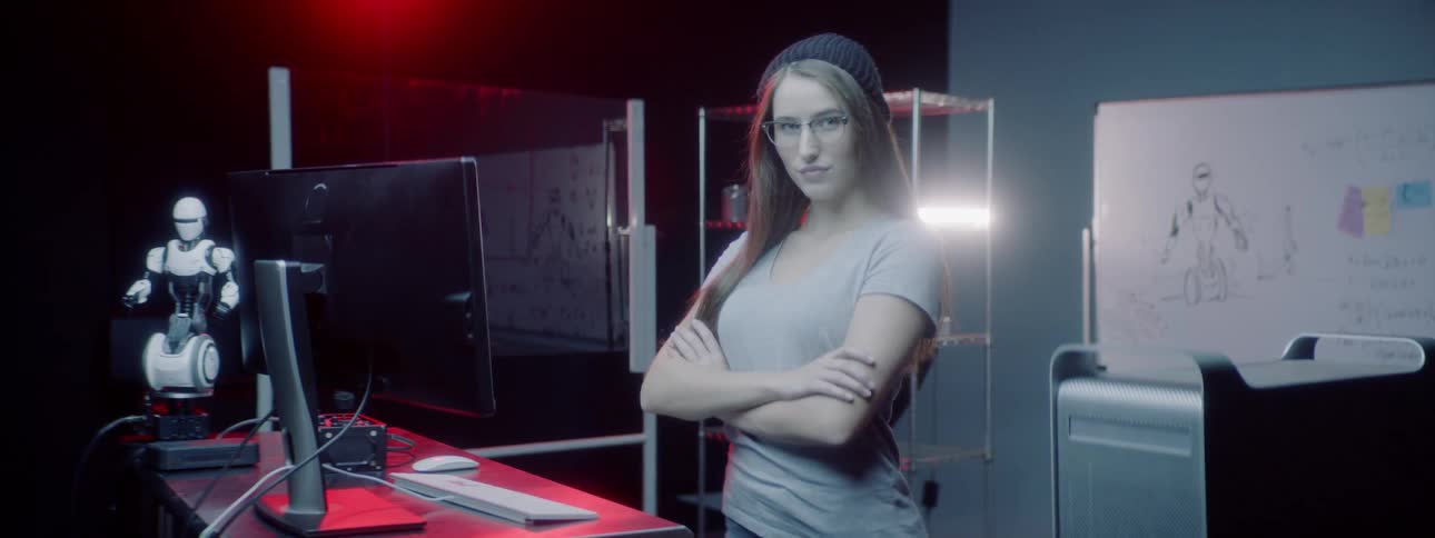 A woman standing in a computer lab crosses her arms to pose for a portrait