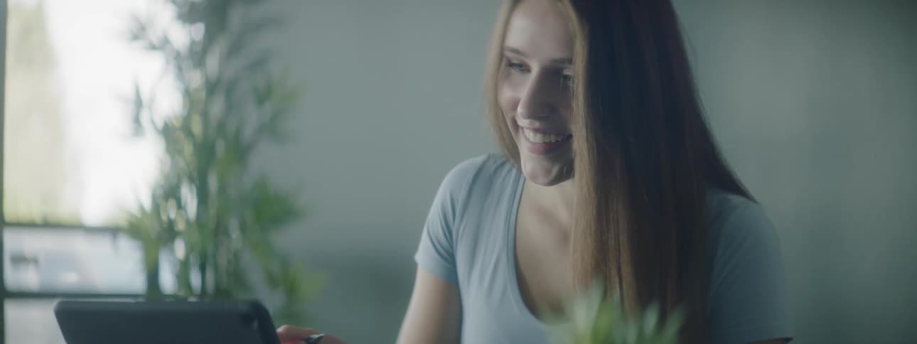 A young girl talks and laughs as she looks at her laptop and writes on paper
