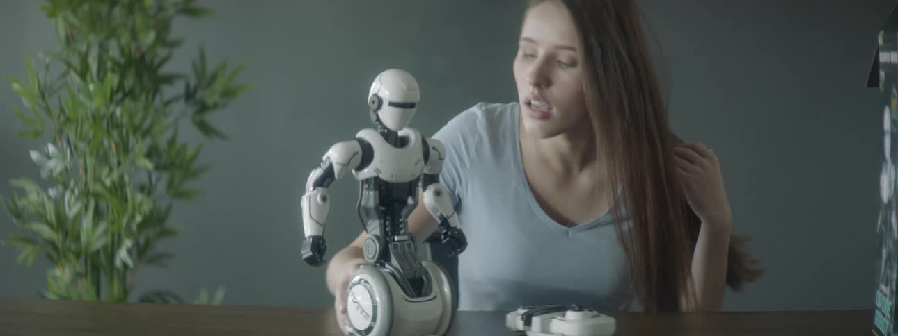 A woman sits at a table and turns on a robot