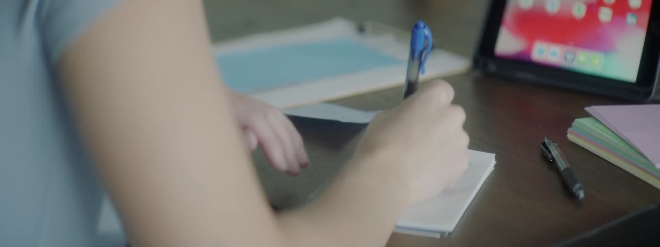 A woman takes notes while sitting at a desk with a tablet