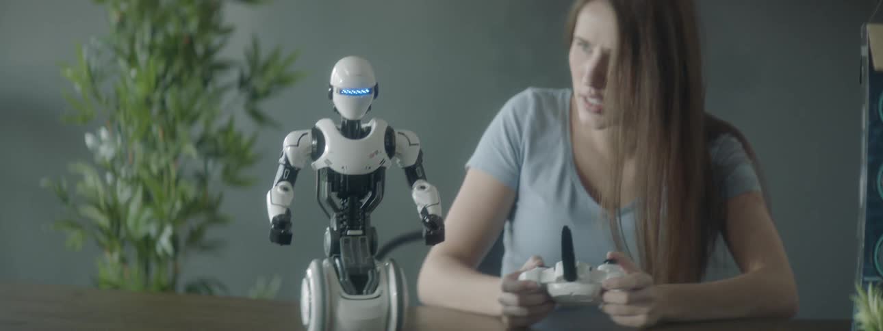 A young woman holds a remote controller that shes using to control a small toy robot