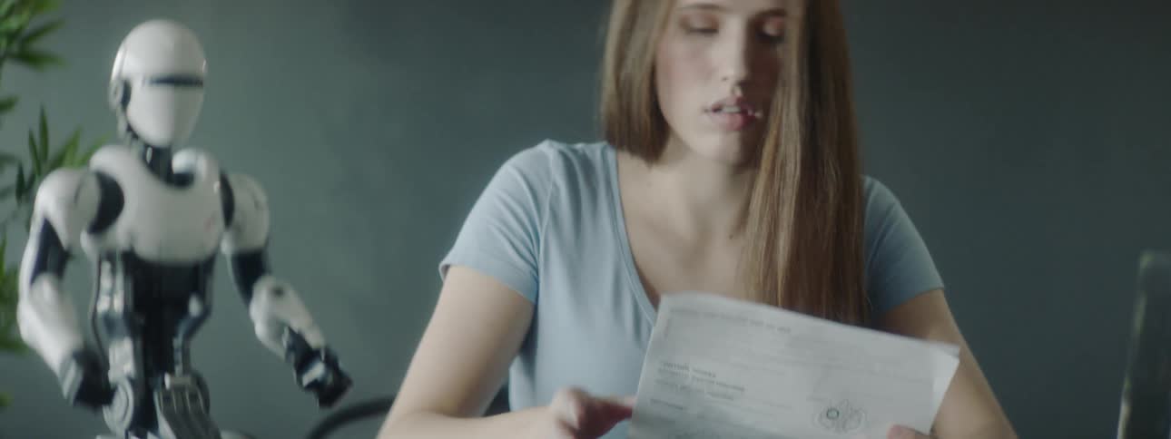 A small robot sits on a table while a woman studies an instruction sheet
