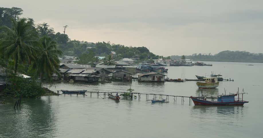 Small fishing boats docked on a tropical coast with village shacks and buildings