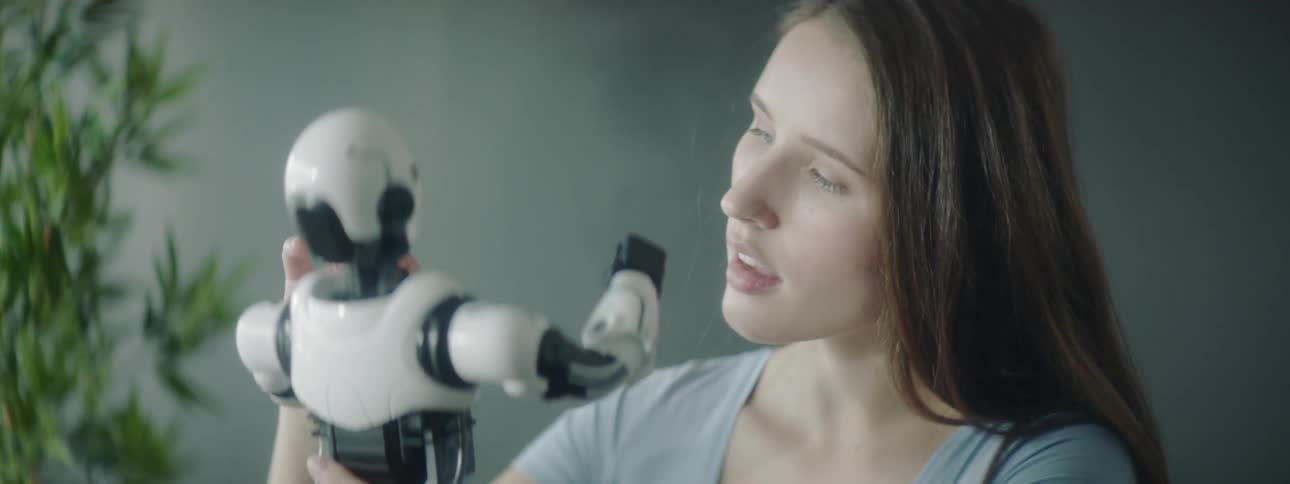 A woman with very long hair holds and inspects a white and black toy robot