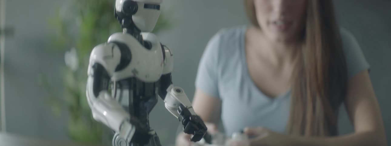A young woman concentrates as she operates a remote control in order to move a small robot