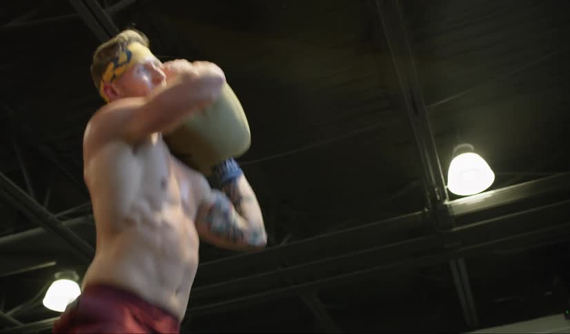 Man lifts sand bag over his shoulders on a gym