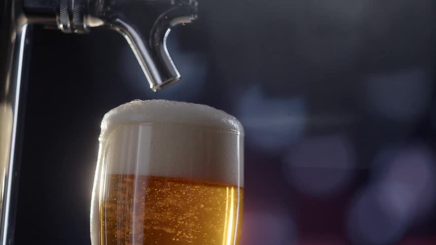 A foaming glass of beer under a beer tap