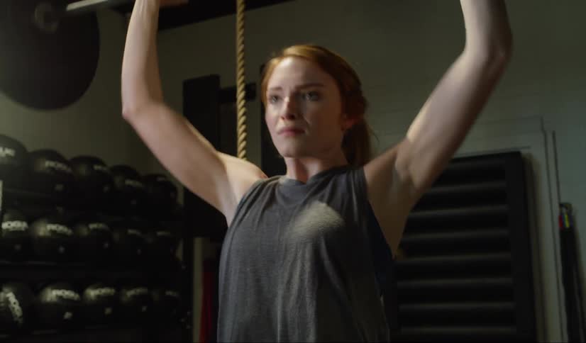 Woman lifts weight bar over head doing reps