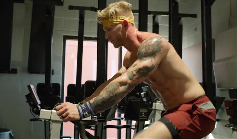 Shirtless male with tattoos working out on an exercise bike indoors
