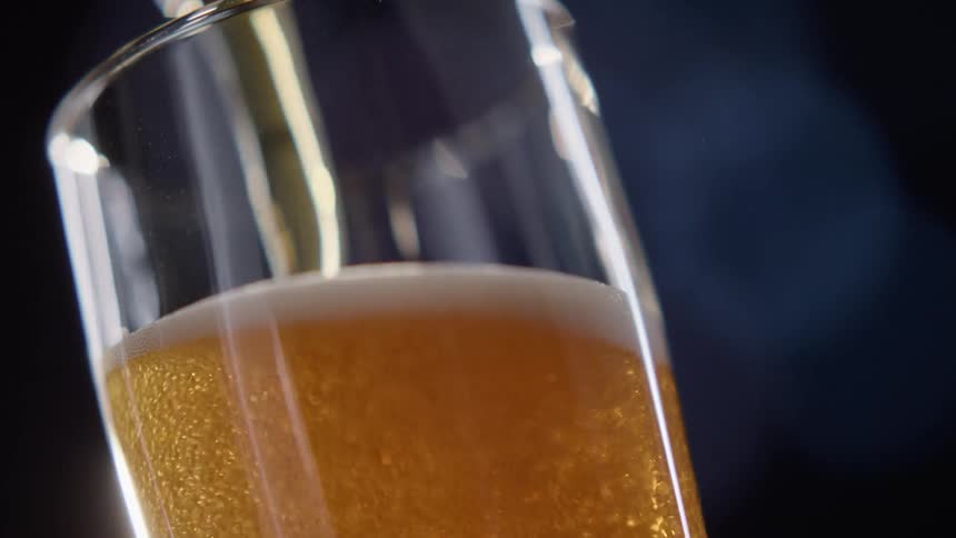 Amber beer flows from a metal tap and foams and bubbles as it fills a glass below