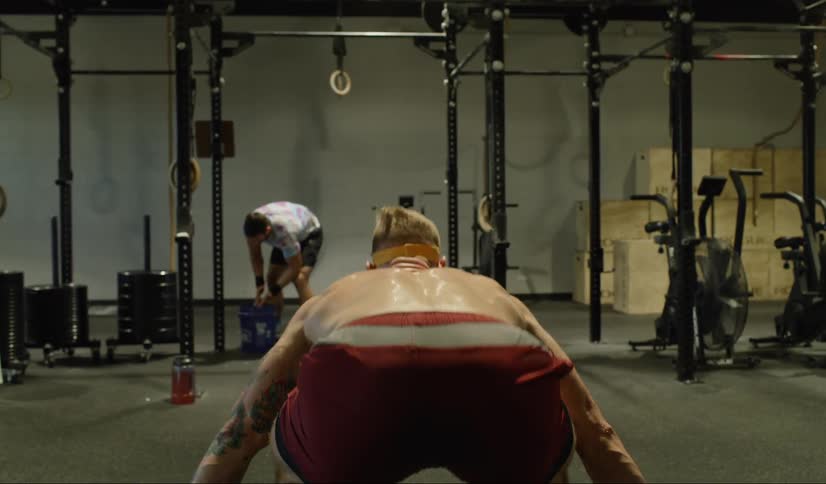 A large muscular man covered in sweat forcefully raises an olympic bar with large weights over his head