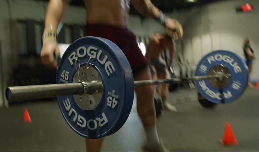 A muscular young man lifts an olympic bar from the ground and raises it over his head before throwing it back down