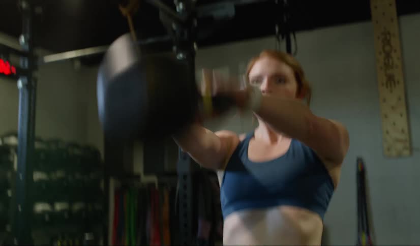 A woman works out with a kettlebell in a gym near weights