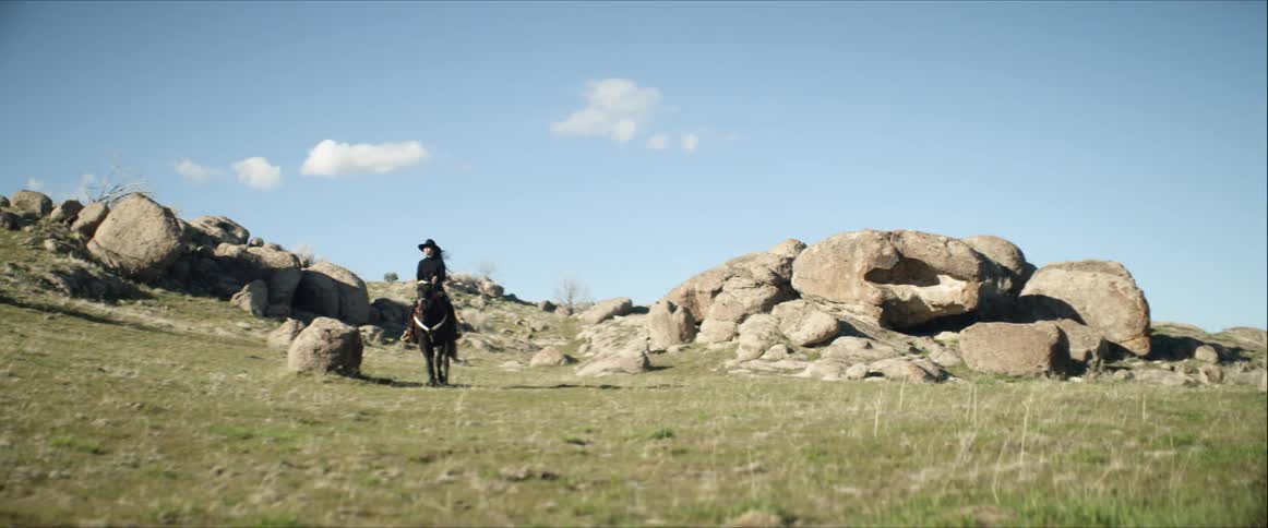 A woman rides a horse through a field strewn with huge boulders