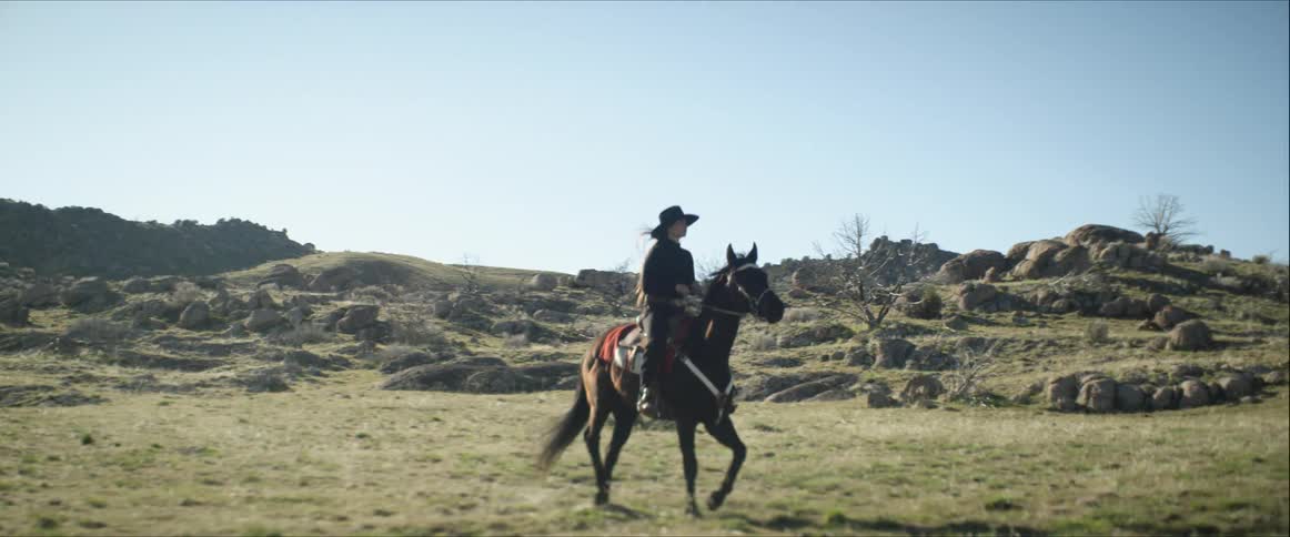 White woman riding a horse across an empty field