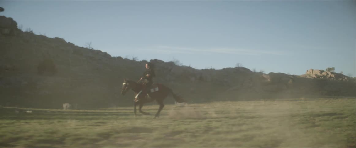 White woman riding a horse across a field