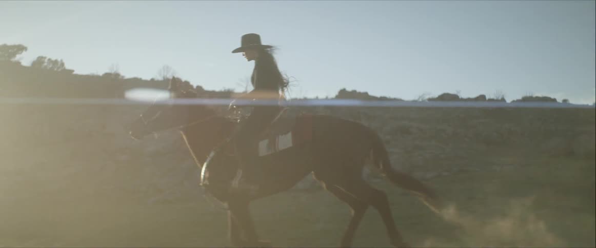 A young woman rides atop a swiftly galloping horse through a rocky wilderness area