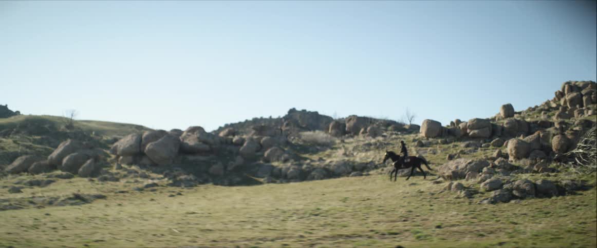 Cowgirl rides horse through rock littered hillside