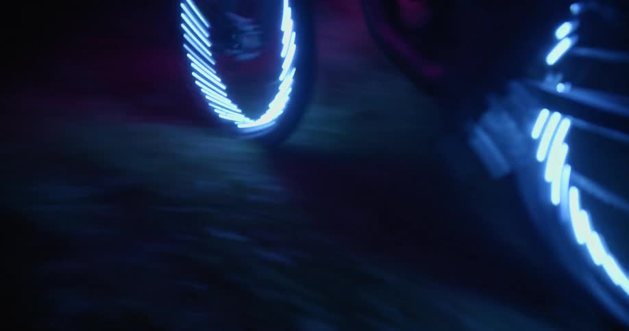 A person rides a bike with bright blue lights fixed to the wheels through a dark forest