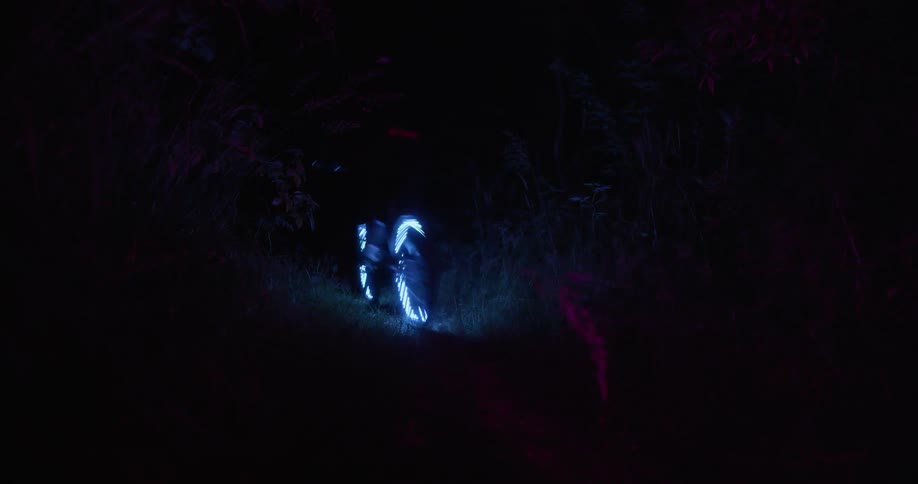 Person rides bicycle with glowing tires along grassypath outdoors