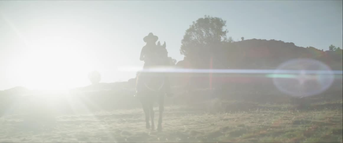 A woman in a cowboy hat rides on the back of a horse through a outdoor field