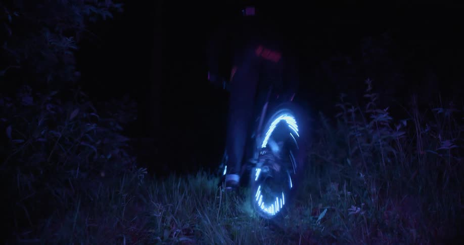 A boy rides his bike with lit up wheels at night
