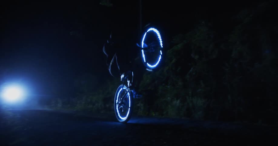 A person pops a wheelie on his bike at night