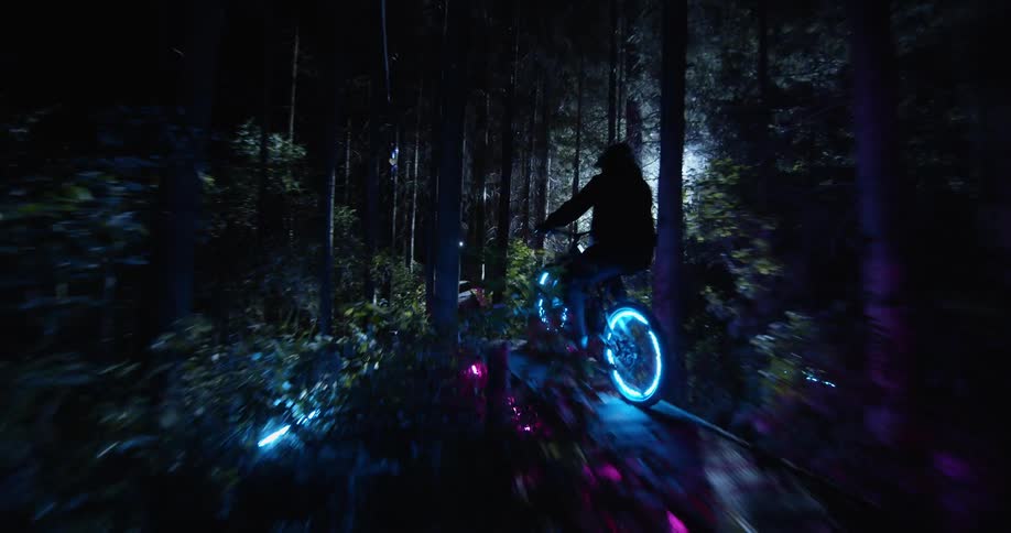 Person riding a bike on forest trail at night with spoke lights